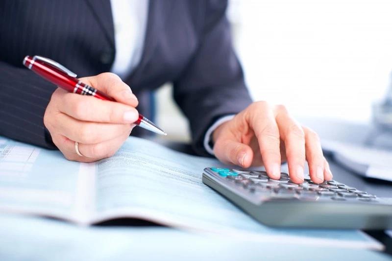 person holding a pen and with hand on calculator at a desk